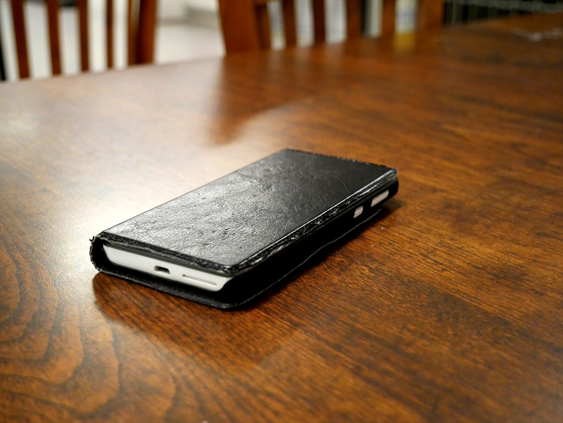 Bílý telefon v zavřeném černém pouzdře leží na dřevěném stole.